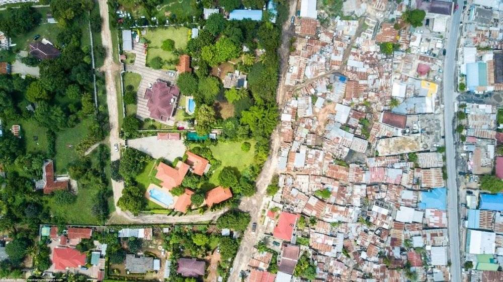 坦桑尼亚达累斯萨拉姆。2012年，该市约有70％的人口居住在这样的贫民窟，该贫民窟位于Mikocheni北郊。左边是曾经属于英国和德国富裕殖民者的富裕土地，现在有大片的豪宅，而右边是Msasani贫民区。摄影：Johnny Miller，图片来源：IC photo