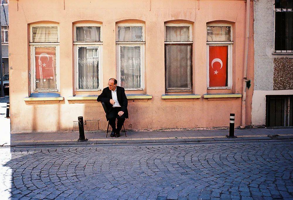贝伊奥卢区，一个男人坐在两面星月国旗之间，悠闲地抽着烟。<br>