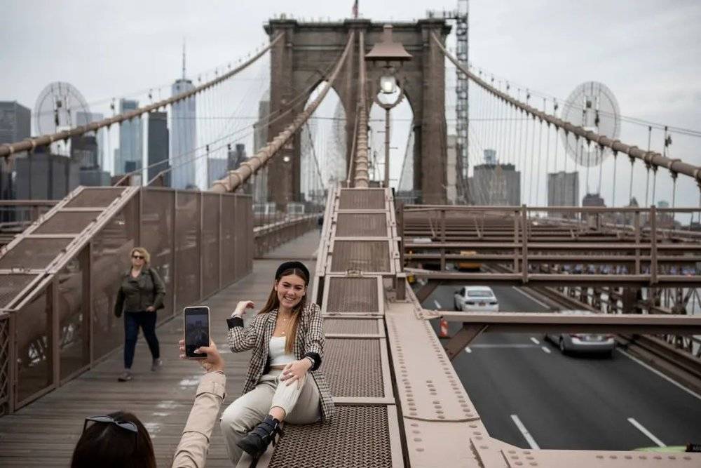 一位来自墨西哥的游客在布鲁克林大桥上拍照。纽约市的游客人数从2019年的6600万锐减至去年的2200万。©Kirsten Luce/《纽约时报》<br>