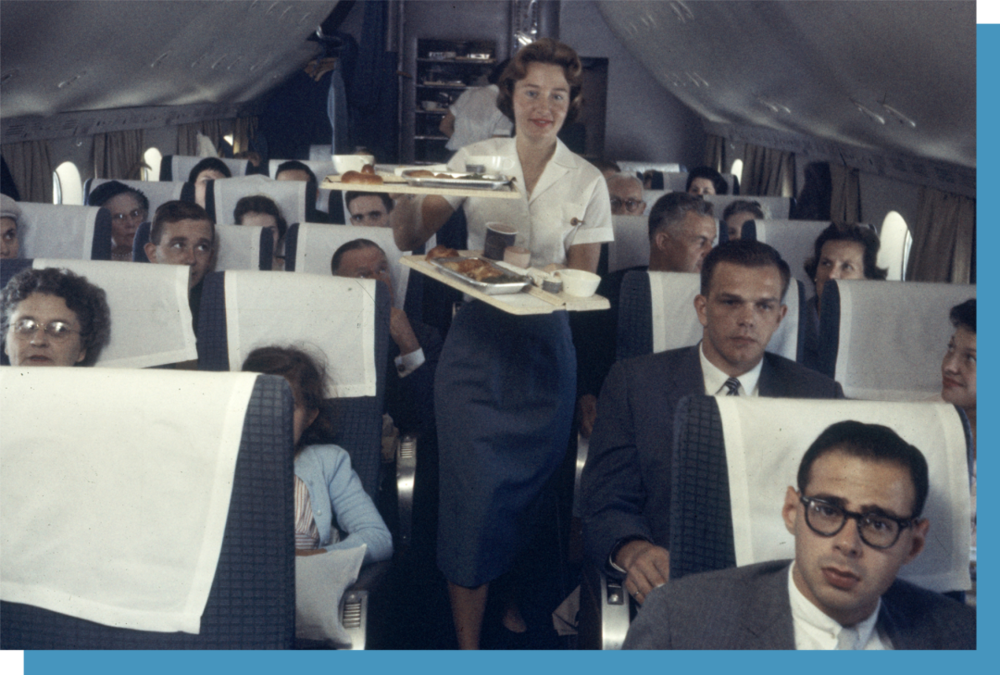 1958 年，泛美航空公司的一名乘务员在飞机上用托盘为乘客提供食物。© Peter Stackpole