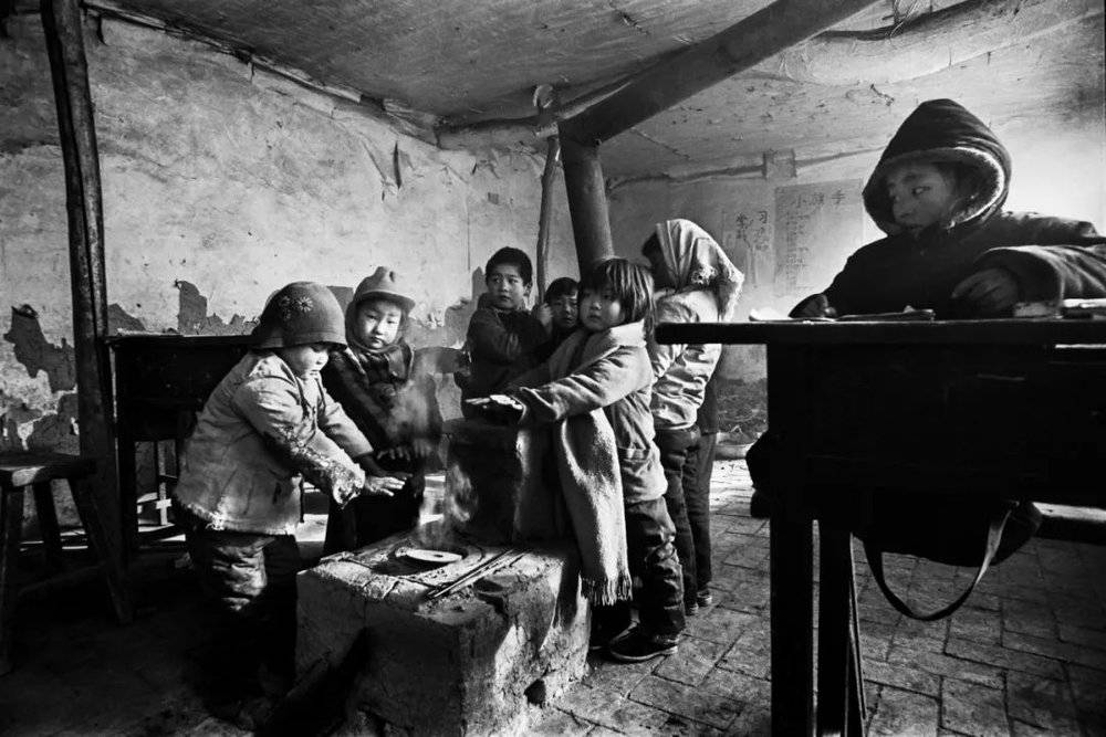 1991年12月的某个冬日，气温骤降至零下20摄氏度，在河北省滦平县拉海沟乡大店子村小学课堂上，孩子们烤烤冻僵的小手继续上课。摄影/解海龙