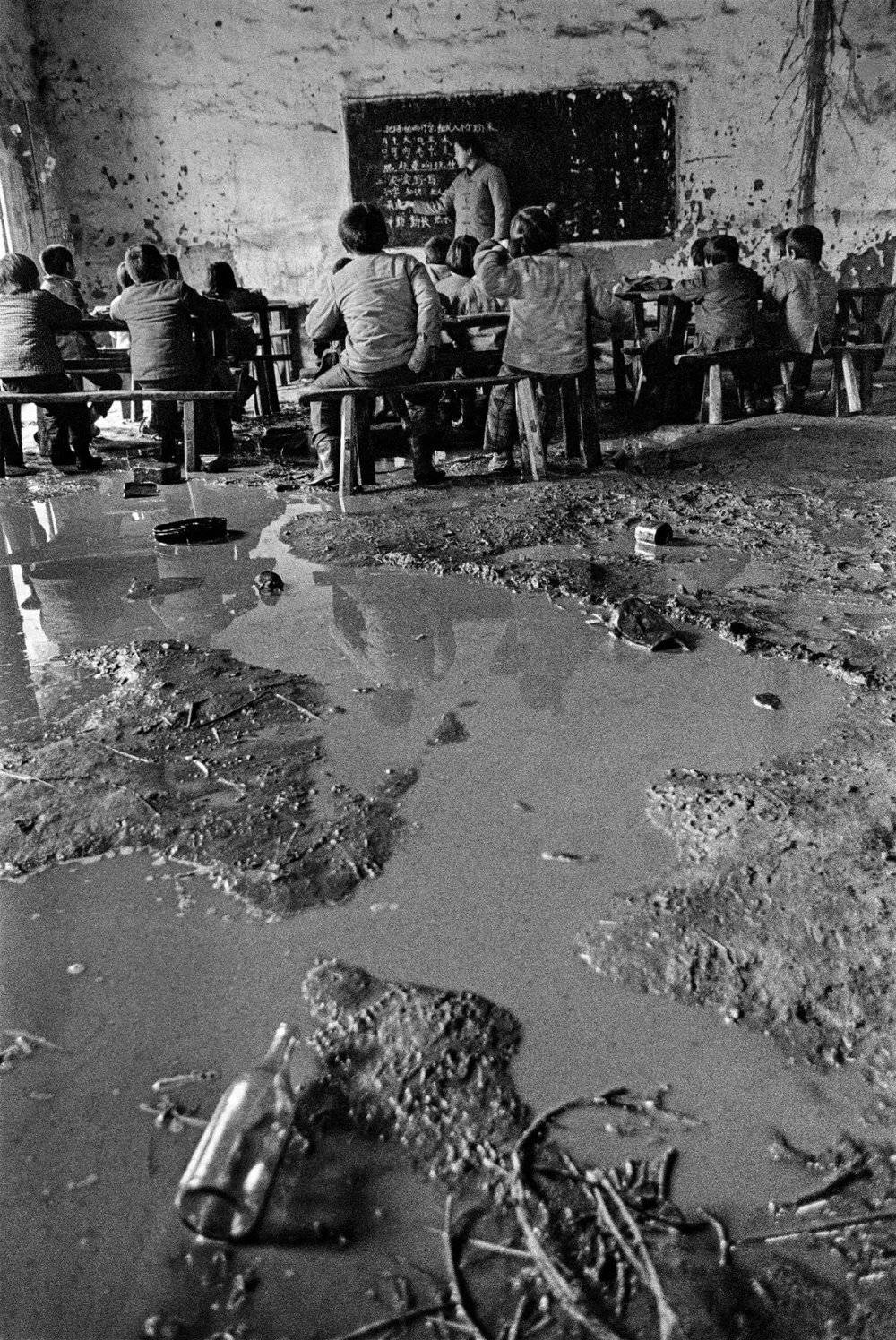 1991年 4月，一场春雨造成湖北省红安县七里坪镇周七家小学教室一片泥泞，孩子们集中在前排继续上课。摄影/解海龙