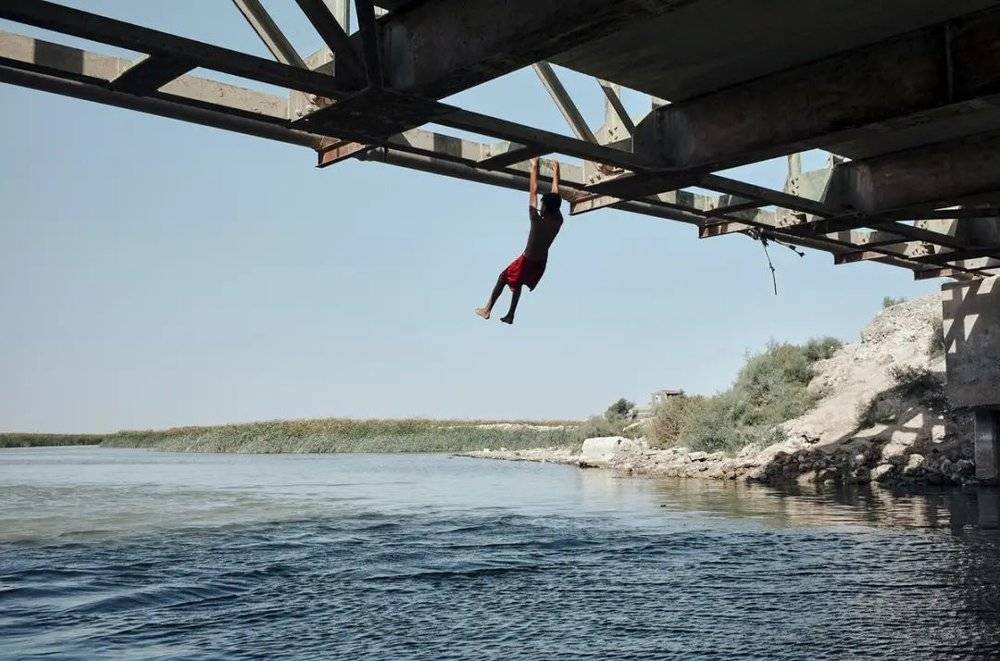 伊拉克大沼泽，一个男孩抓着铁桥准备跳水