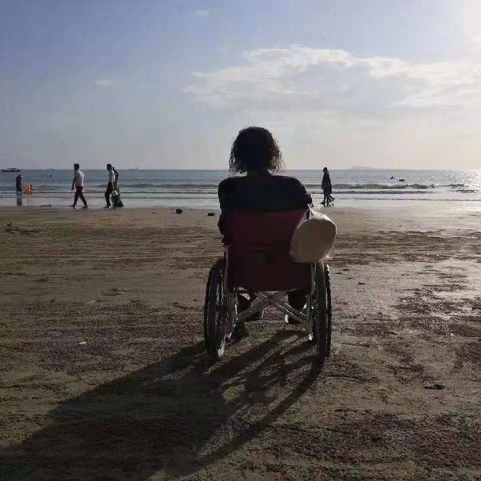 2021年初春，赵已然在三亚海边。轮椅上挂着他喜欢的馕，赵已然后来用这张图当了头像。 摄影/崔弋鑫<br>
