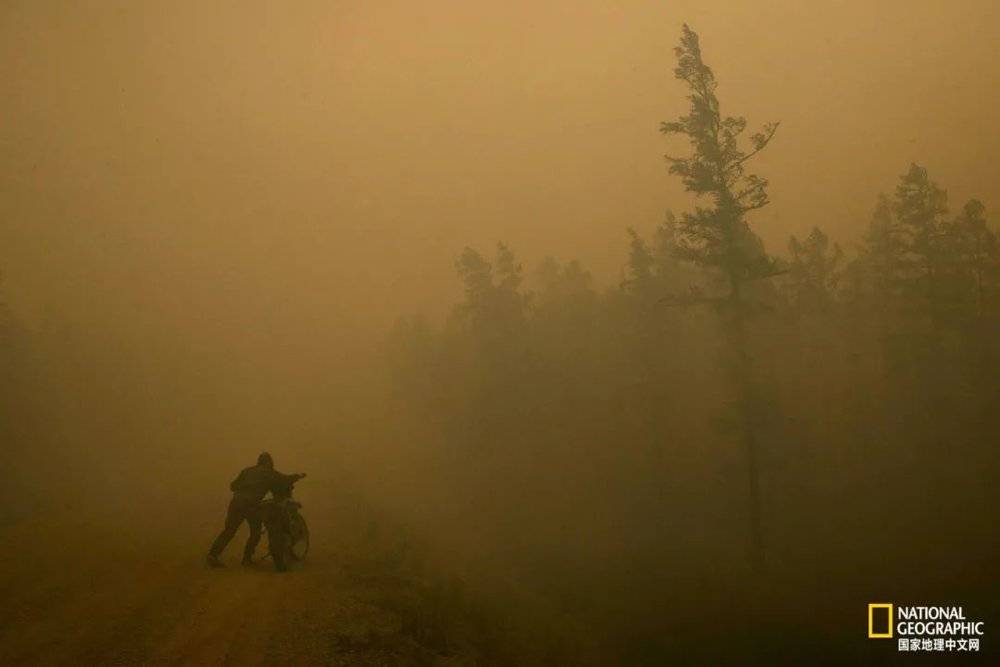 在俄罗斯东北部、萨哈共和国的Kyuyorelyakh，距离图中不到400米的地方正在发生火灾，37岁的志愿消防员Oleg Shcherbakov正推着摩托车穿过浓烟，赶往救援。<br>