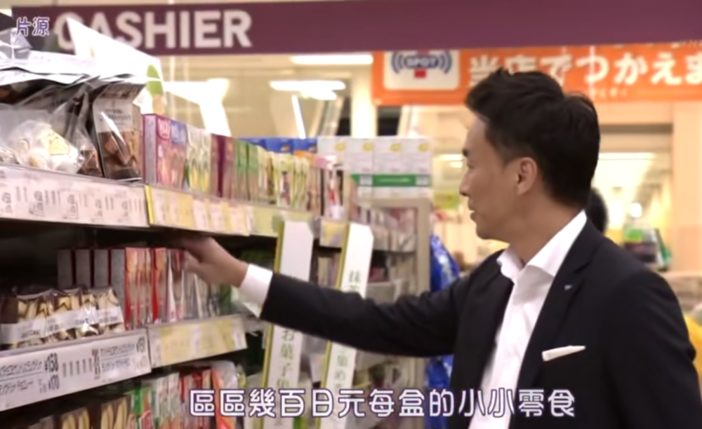 小林正典在超市零食货架旁看自家产品，图片来源：NHK纪录片《零食王国的热销品》截图
