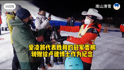 今年1月1日，谷爱凌在自由式滑雪世界杯卡尔加里站U型场地夺冠，将标志着冠军胜利的香槟酒赠予去现场加油的卢建。图片截自南山滑雪视频。
