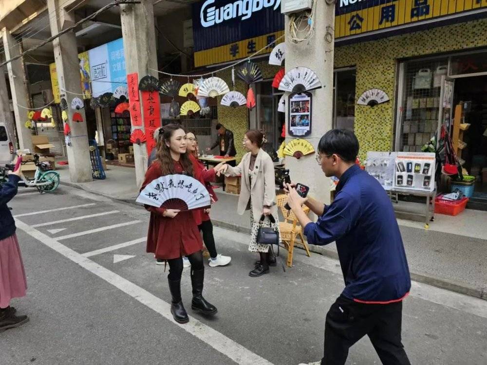 一位游客，举着“老默我想吃鱼了”的折扇，在“强盛小灵通”门店前拍照打卡 陈熊海摄