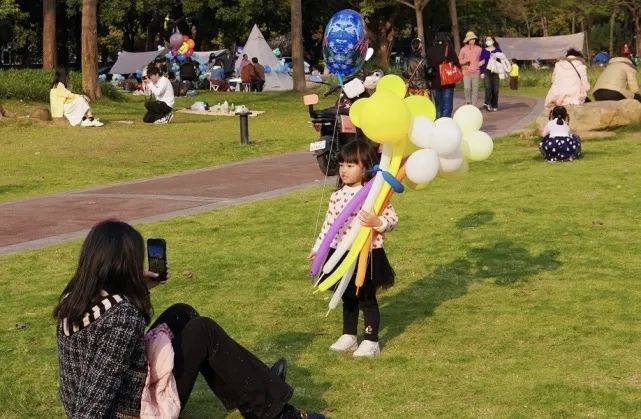 女孩抱着比自己还大的气球花束，拍照留念，阳光把她的影子拉得长长的。时代财经王莹岭摄