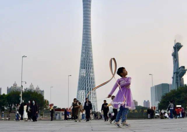 在游人如织的花城广场，广州塔下，一个小女孩忘我地挥舞着彩带，面对来往的人群，她如入无人之境。时代财经王莹岭摄