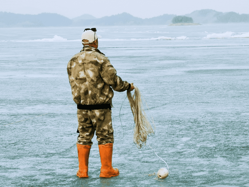 图 | 渔民郭小超在冰面上收拾捕鱼工具。摄影：施安<br>