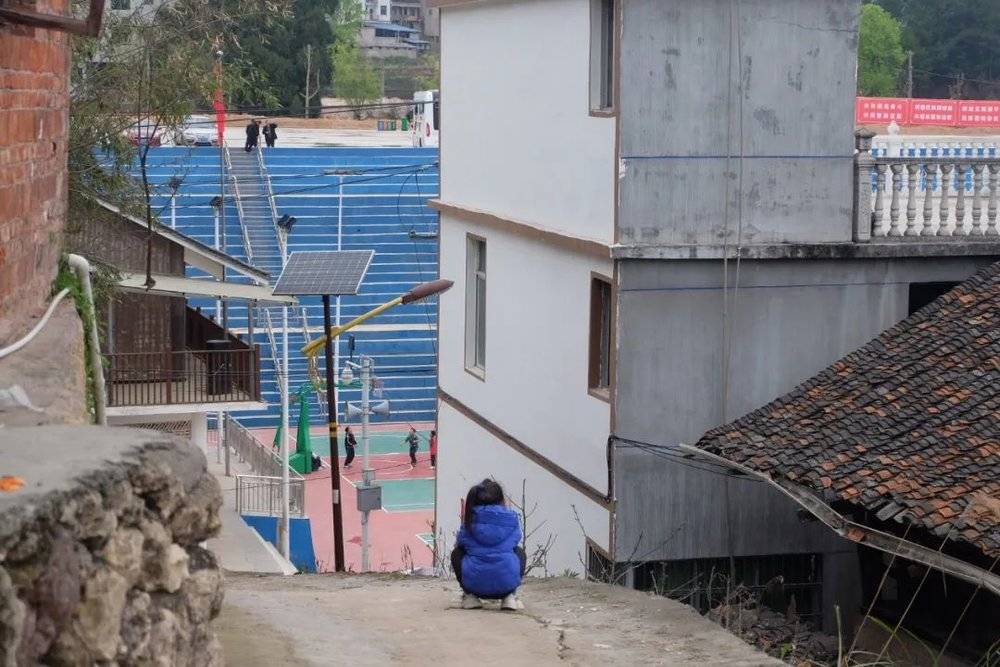 台盘村，一个小女孩蹲着眺望篮球场。图/新周刊记者摄<br>